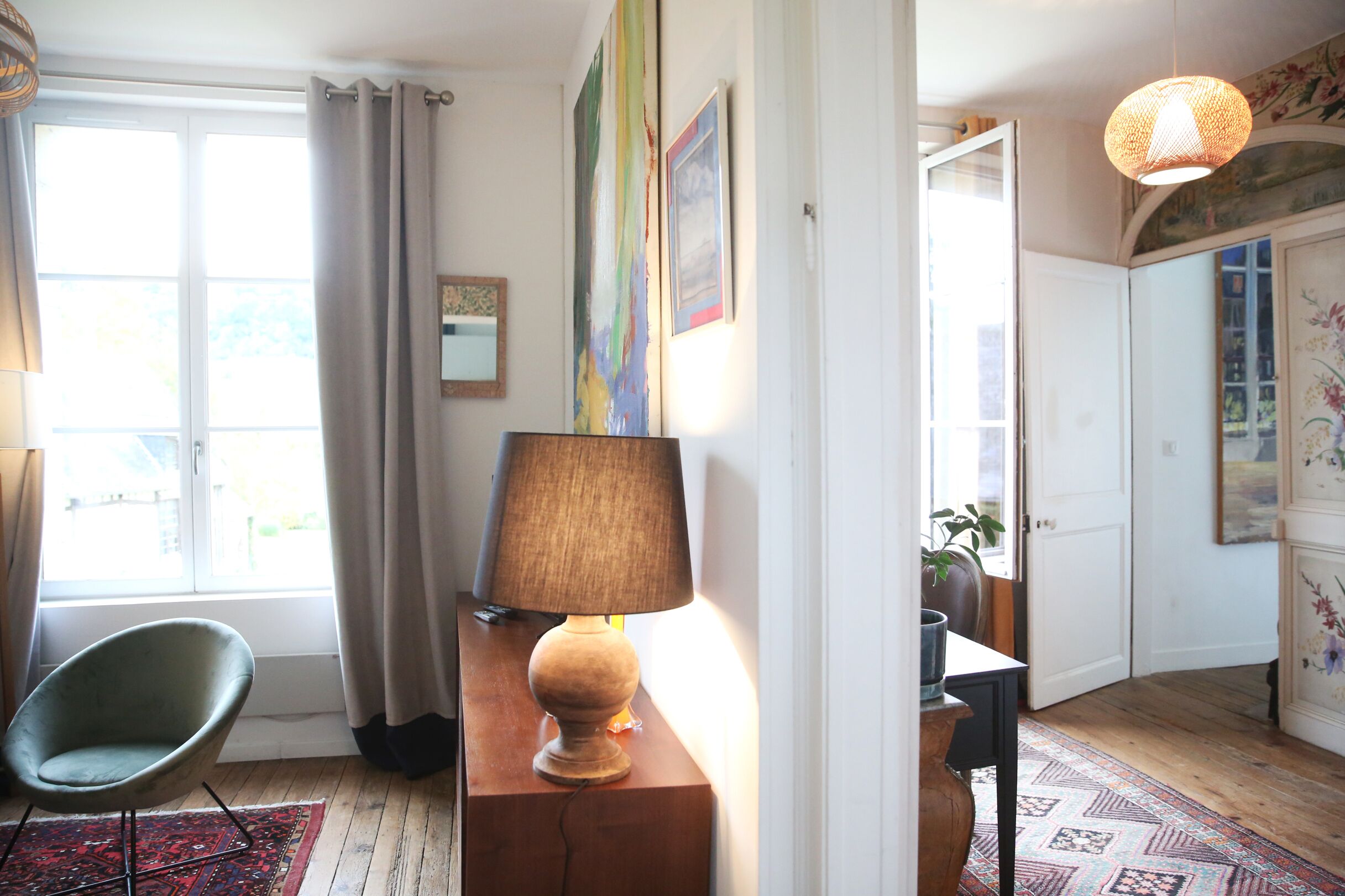 Een kamer met een stoel, een lamp, een vloerkleed en een deur die naar een andere kamer leidt.