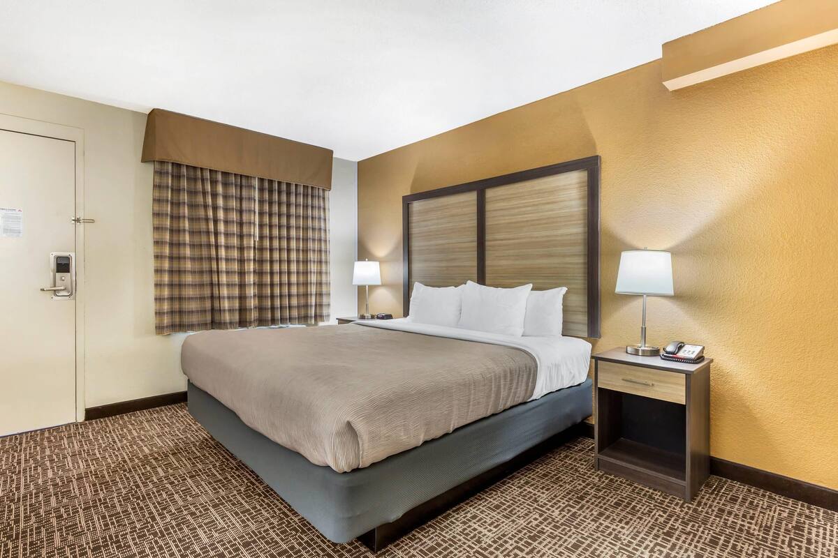 A hotel room with a bed, bedside tables, a nightstand, a lamp, a telephone, and a door.