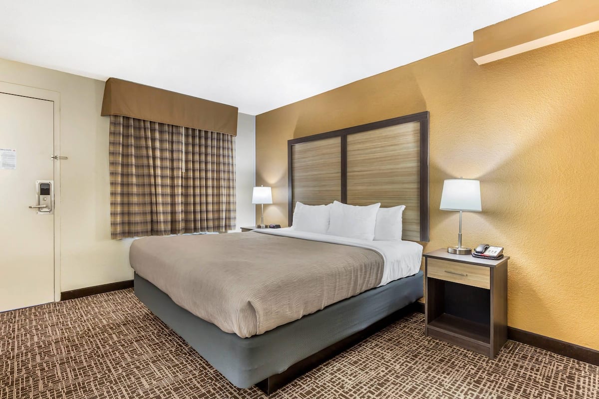 Habitación de hotel con cama, mesitas de noche, lámpara, teléfono y puerta.