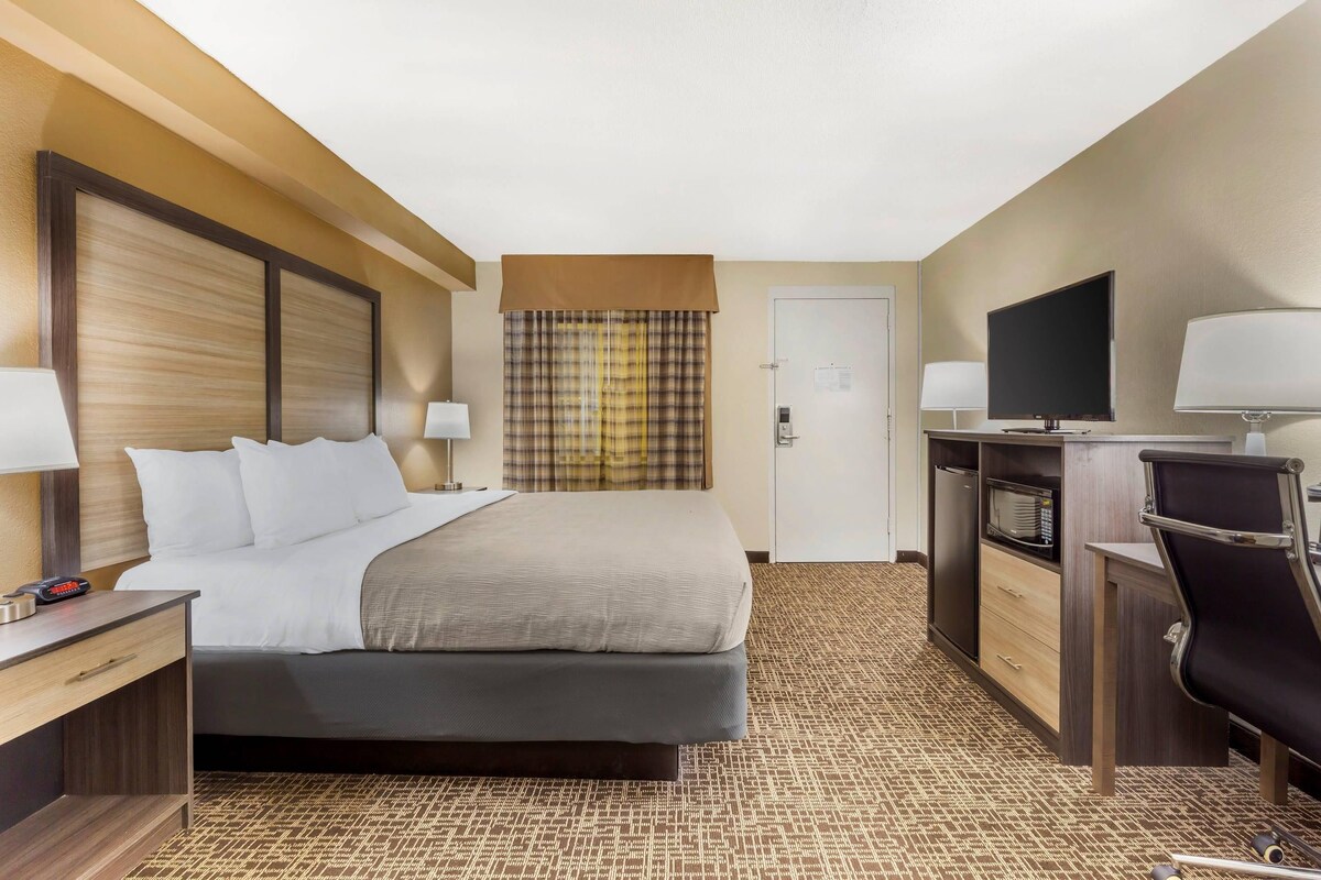 A hotel room with a bed, bedside tables, a desk, a television, and a wardrobe.