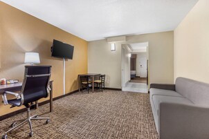A hotel room with a desk, chair, TV, and a sofa.