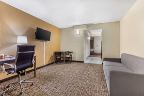 A hotel room with a desk, chair, TV, and a sofa.