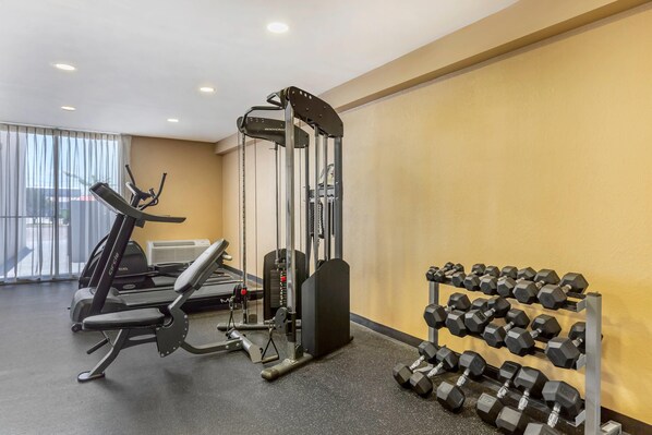 A gym with cardio equipment, weight benches, and a rack of dumbbells.