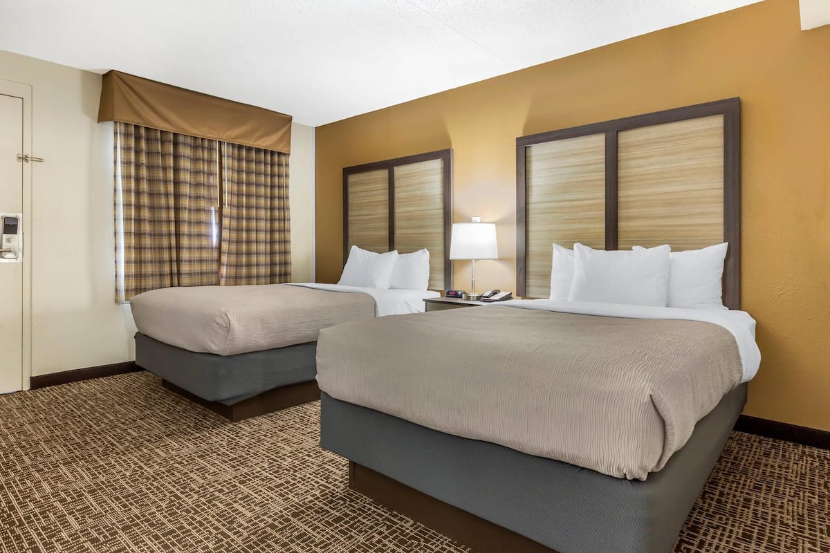 Habitación de hotel con dos camas, una mesa de recepción, un teléfono y una ventana con cortinas.