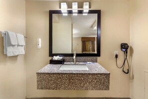 A bathroom with a granite countertop sink, a large mirror, a towel rack, and a hairdryer on the wall.
