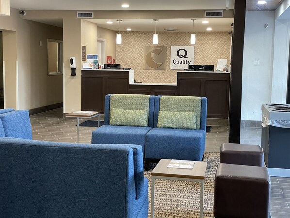 A hotel reception area with a blue sofa, a small table, and a counter with a 'Quality by Choice Hotel' sign.