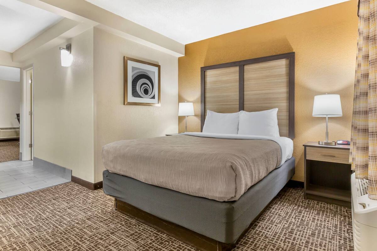 A hotel room with a bed, a nightstand, a lamp, and a painting on the wall.