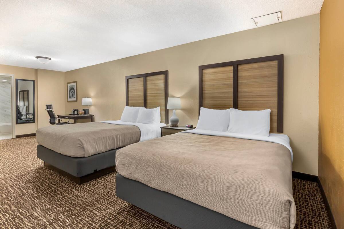 A hotel room with two beds, a desk, a chair, and a mirror.