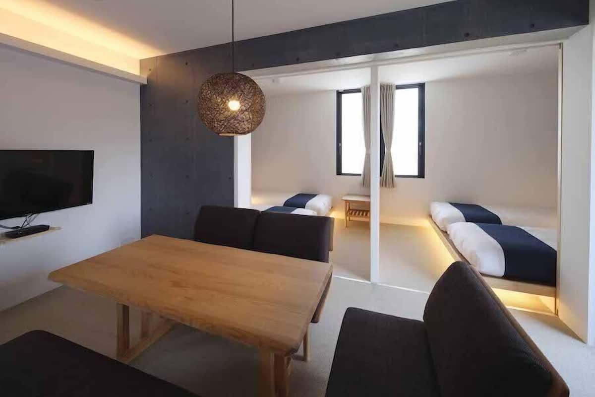 Una sala de estar moderna con una mesa de madera, sofás oscuros, un televisor y una lámpara con una textura singular.