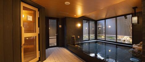A modern indoor pool area with a glass door entrance, tiled flooring, and a view of the outdoors through large windows.