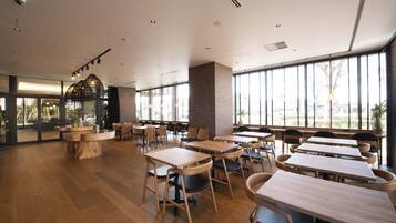 A spacious indoor area with multiple wooden tables and chairs, large windows providing natural light, and a brick column.