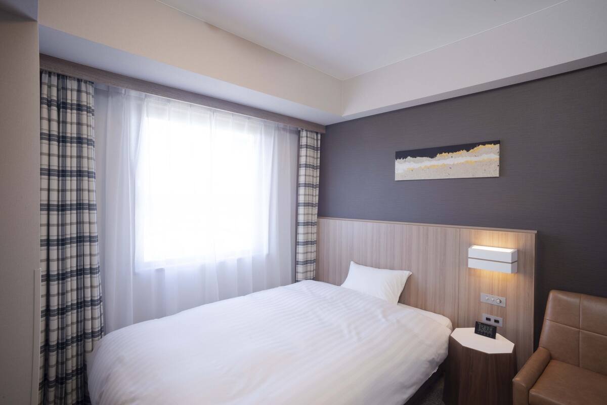 Ein Hotelzimmer mit einem großen Bett, einem Nachttisch mit Lampe, einem Sessel und einem Bild an der Wand.