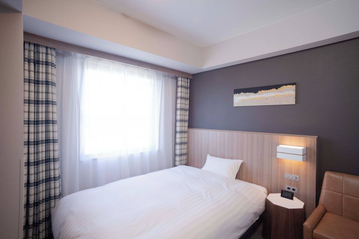 Ein Hotelzimmer mit einem großen Bett, einem Nachttisch mit Lampe, einem Sessel und einem Bild an der Wand.