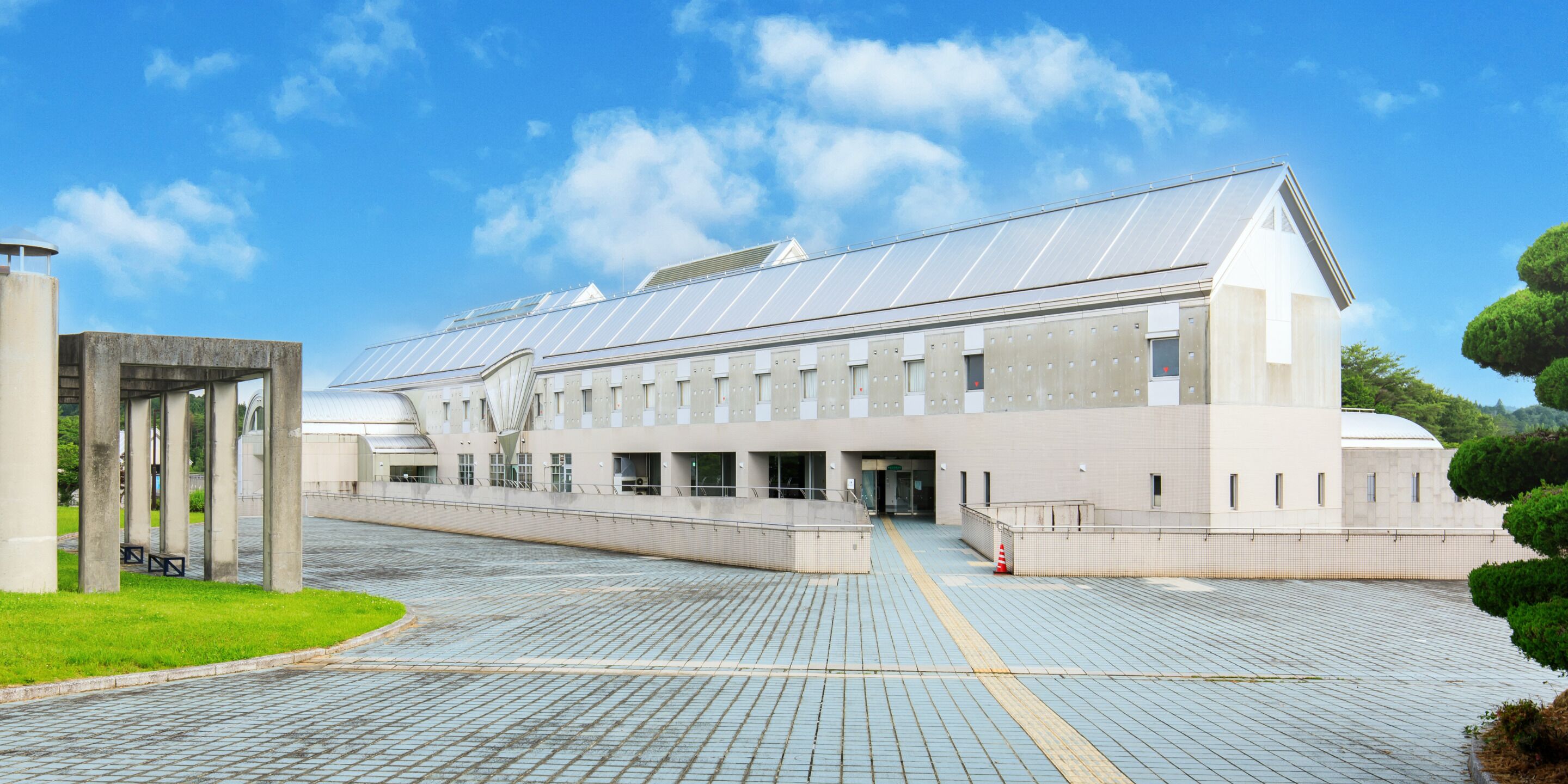 A modern building with a flat roof, large windows, and a paved entrance area.