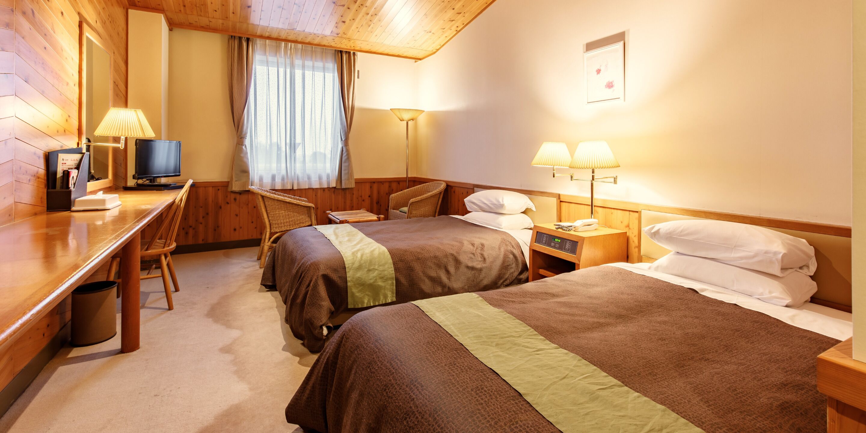 A hotel room with two beds, a desk, a chair, a television, and lamps.