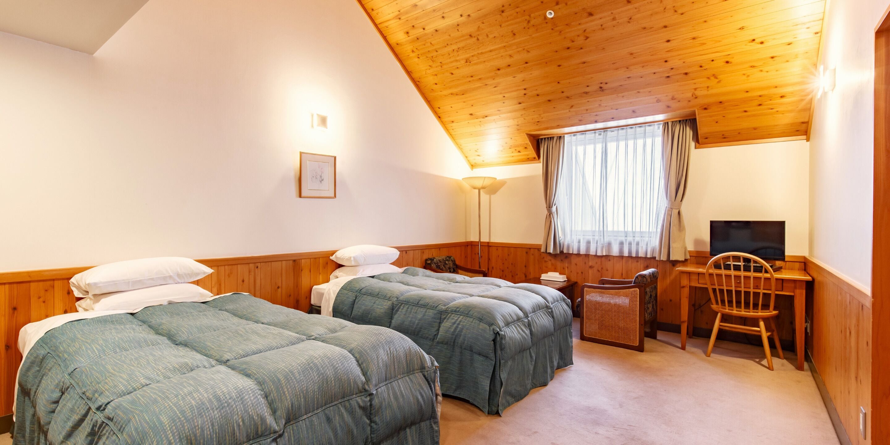 A room with two beds, a desk, a chair, a television, and a window with curtains.