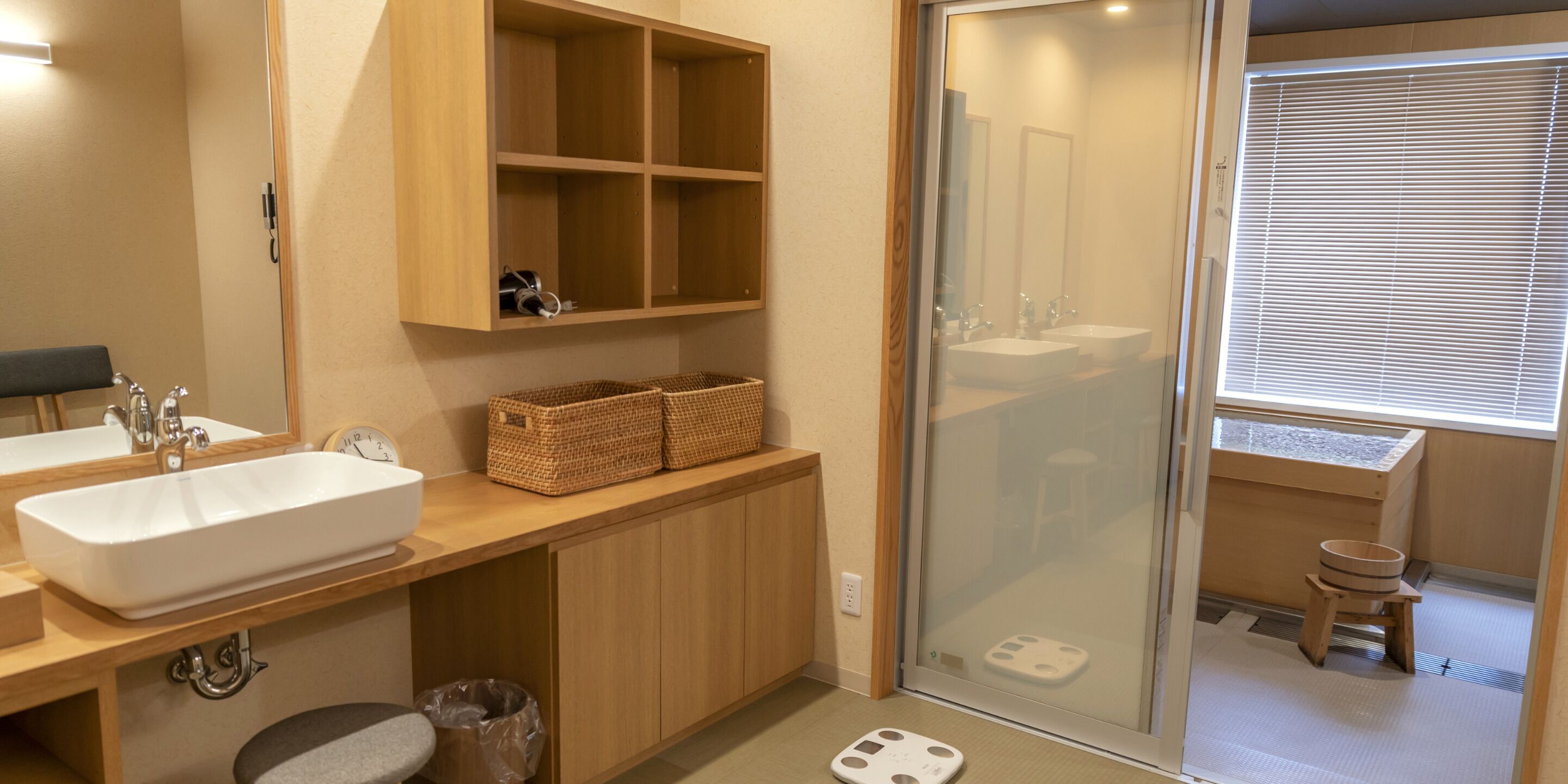A modern bathroom with a large sink, wooden cabinets, a shower area, and a small stool.