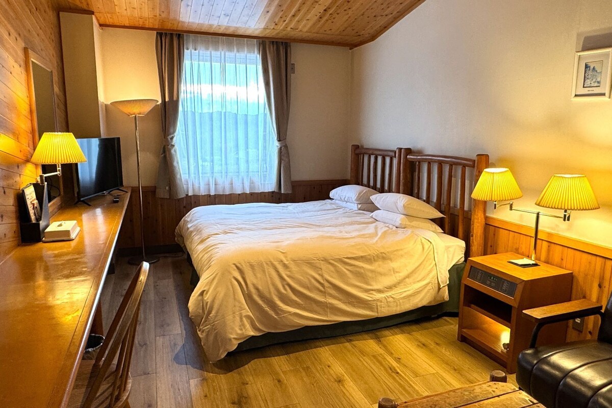 A hotel room with a wooden bed, bedside lamps, a TV, and a wooden desk.