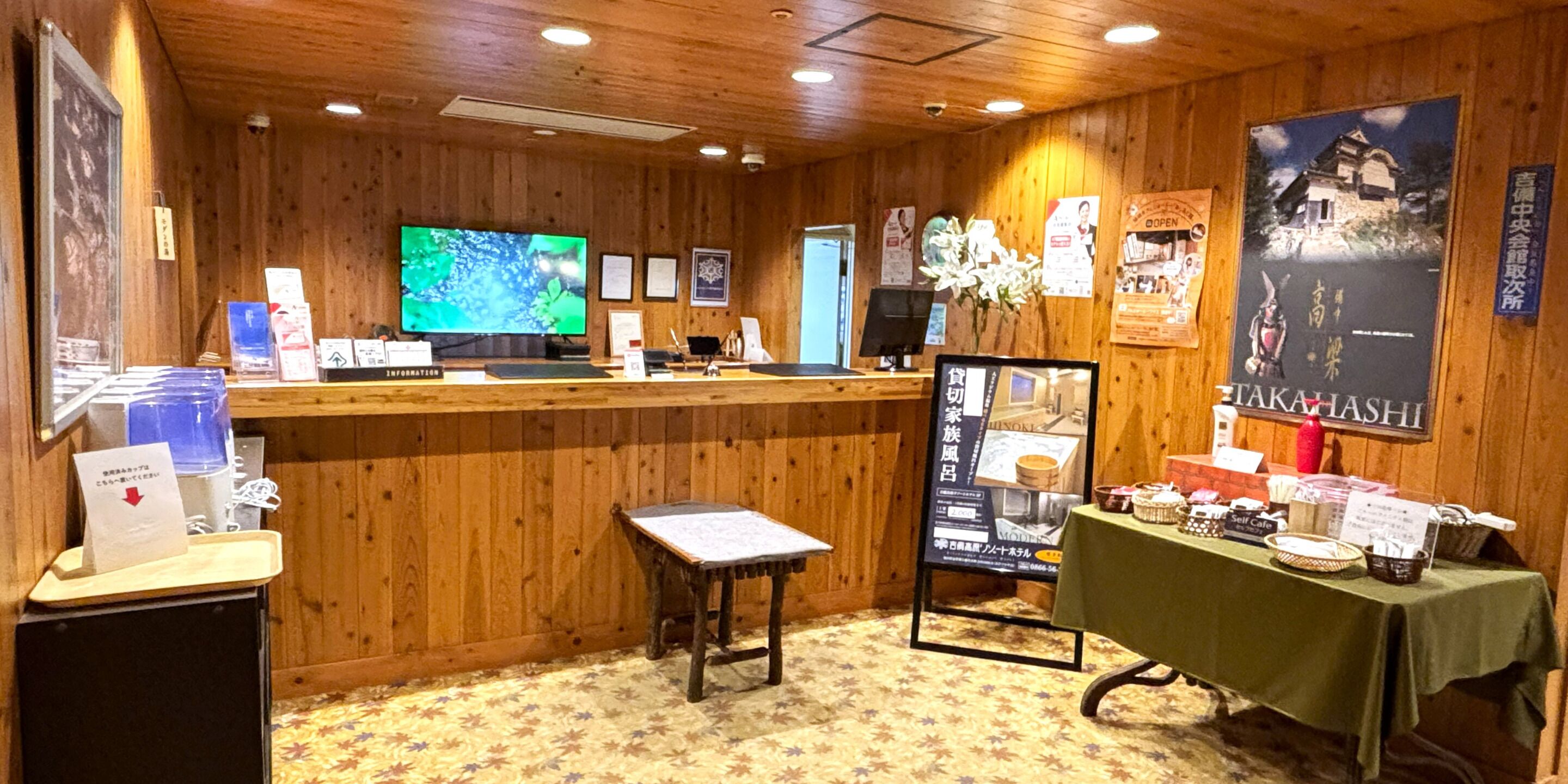 Un intérieur en bois comprenant un comptoir d’accueil, un téléviseur, des affiches d’information et une table sur laquelle sont disposés divers objets.