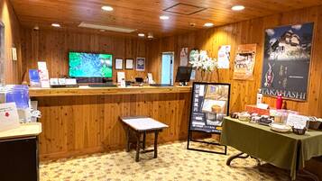Un intérieur en bois comprenant un comptoir d’accueil, un téléviseur, des affiches d’information et une table sur laquelle sont disposés divers objets.