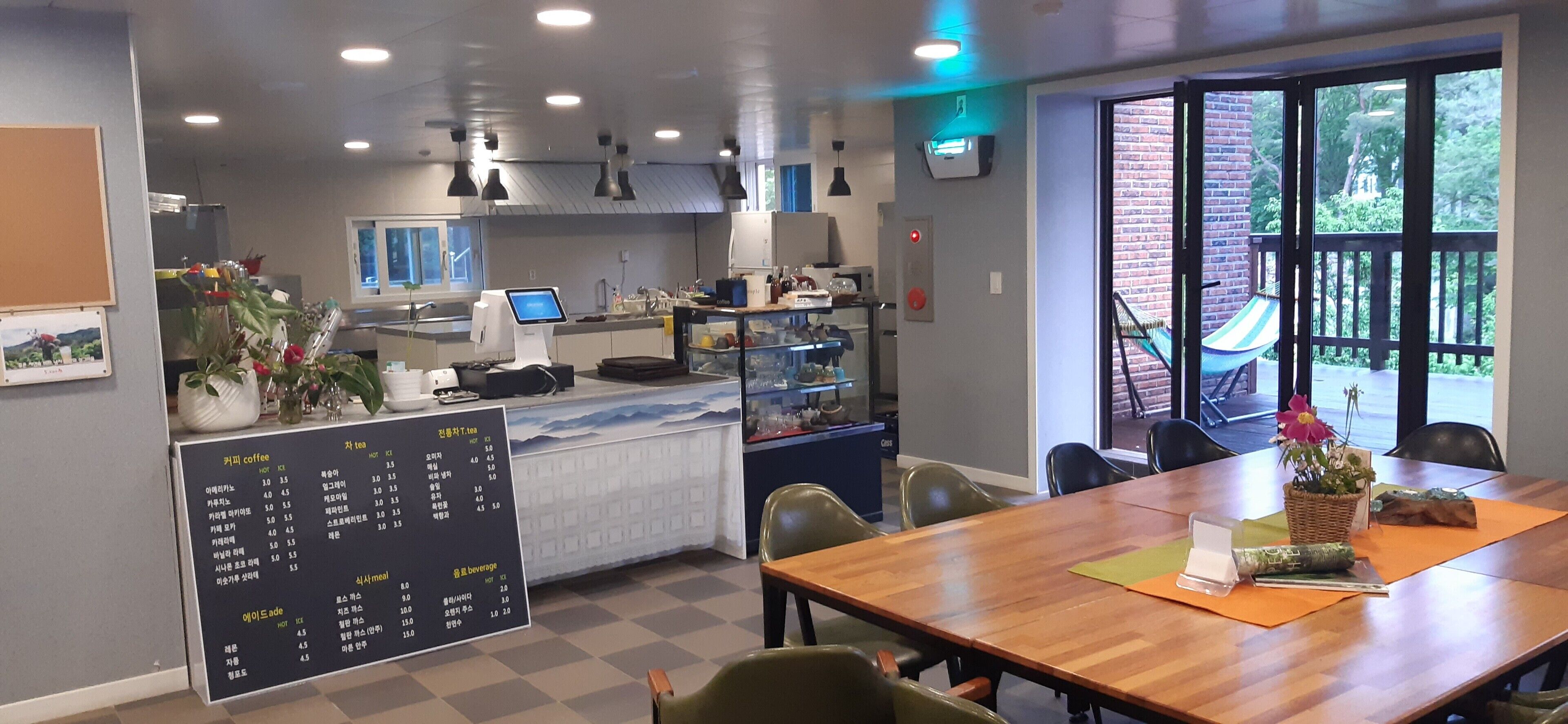 Um café moderno com mesa de madeira, cadeiras, um quadro de cardápio e vista para o exterior.