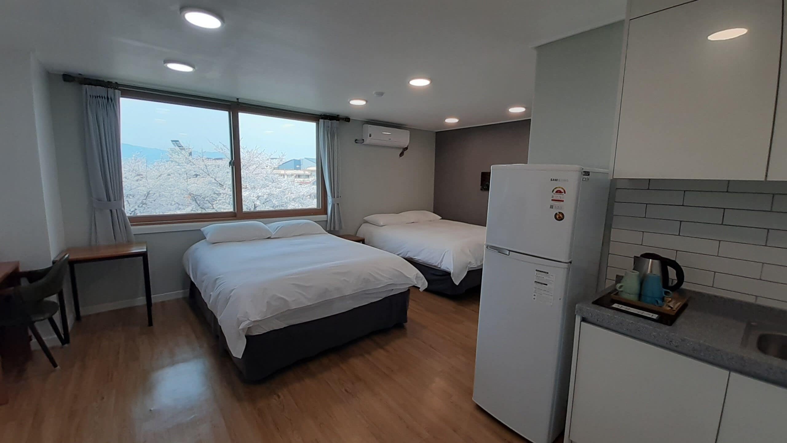 Habitación de hotel compacta con cama, escritorio, kitchenette y ventana con cortinas.