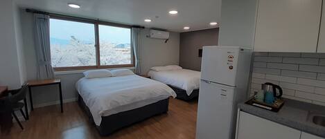 Habitación de hotel compacta con cama, escritorio, kitchenette y ventana con cortinas.