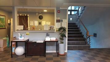 Ein Empfangsbereich mit einem Schreibtisch, einem großen Spiegel, einer Uhr und einer Treppe, die zu einer oberen Etage führt.