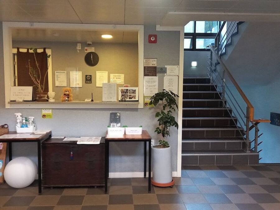 Ein Empfangsbereich mit einem Schreibtisch, einem großen Spiegel, einer Uhr und einer Treppe, die zu einer oberen Etage führt.