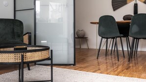 A modern interior with a round table, two chairs, a rattan chair, a decorative fan, and a glass partition. - Nomad's By Sta Catarina Flats - 3BDR Family (Porto)