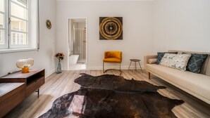 Ein modernes Wohnzimmer mit Ledermatte, einer Couch mit gemusterten Kissen, einem Holztisch und einem Wandkunstwerk.