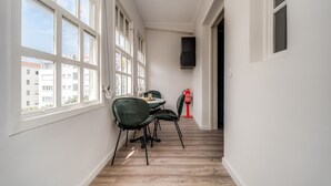 Ein schmaler Flur mit großen Fenstern, einem Tisch mit Stühlen und einem Feuerlöscher.