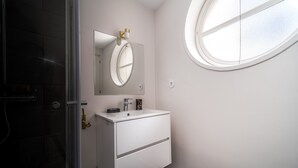 A bathroom with a white vanity, a round mirror, and a window.