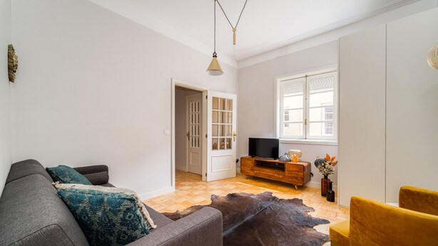 A living room with a sofa, a yellow chair, a wooden TV stand, and a cowhide rug.