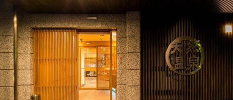Entrada de hotel con puerta corredera de madera, pared de piedra y un letrero con caracteres chinos.