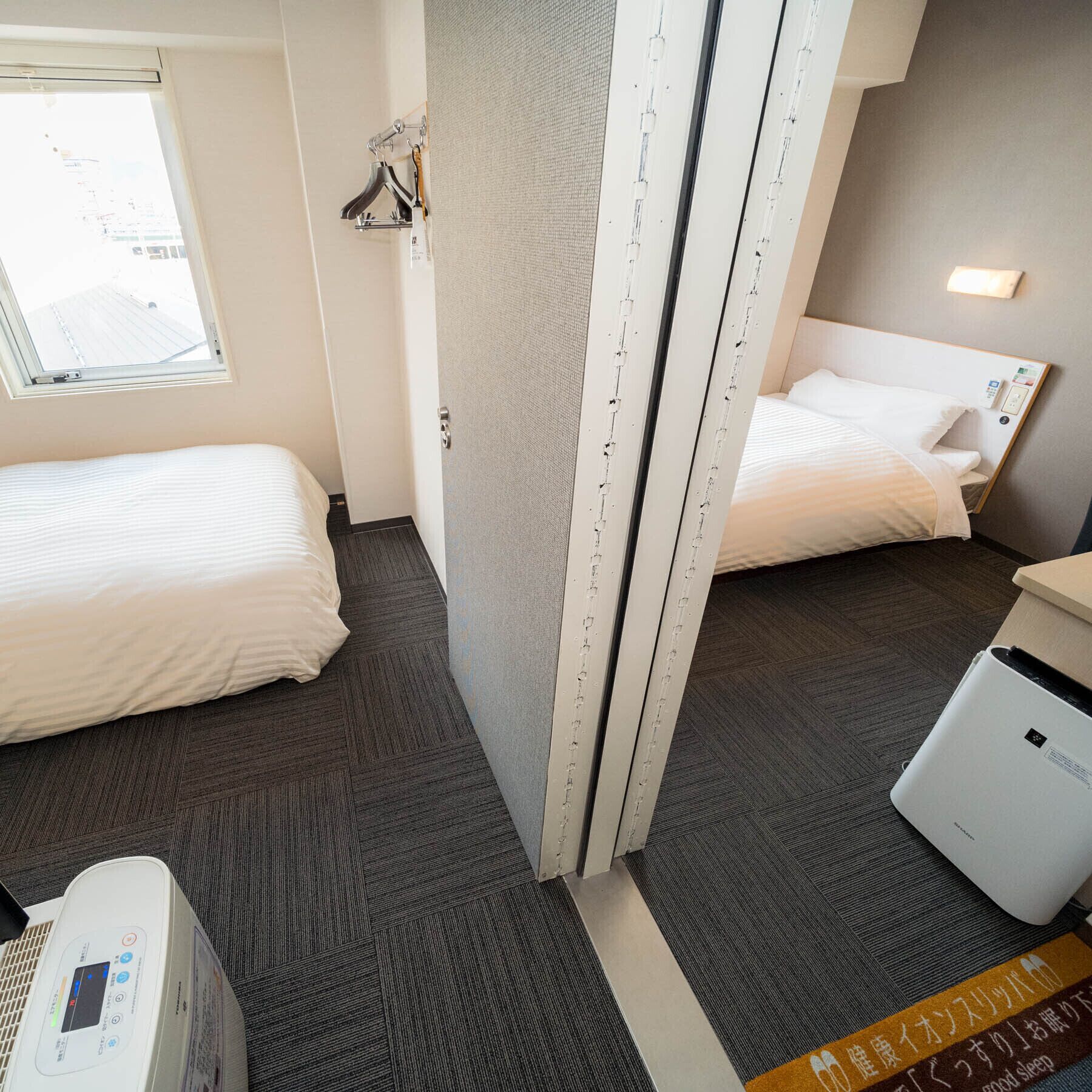 Habitación de hotel con dos camas, una ventana, un calentador y una mesita de noche.