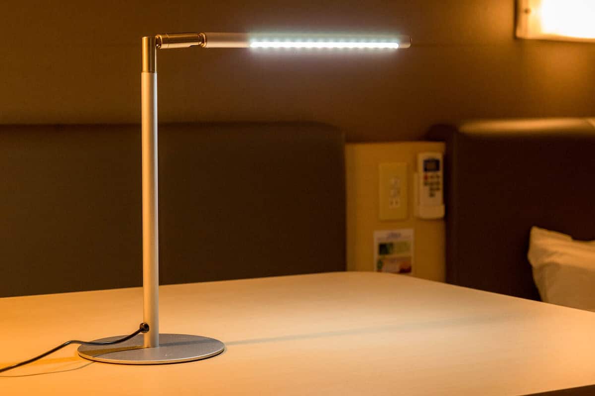 Une chambre d’hôtel équipée d’une table de chevet, d’une lampe, d’un téléphone et d’un luminaire fixé au mur.
