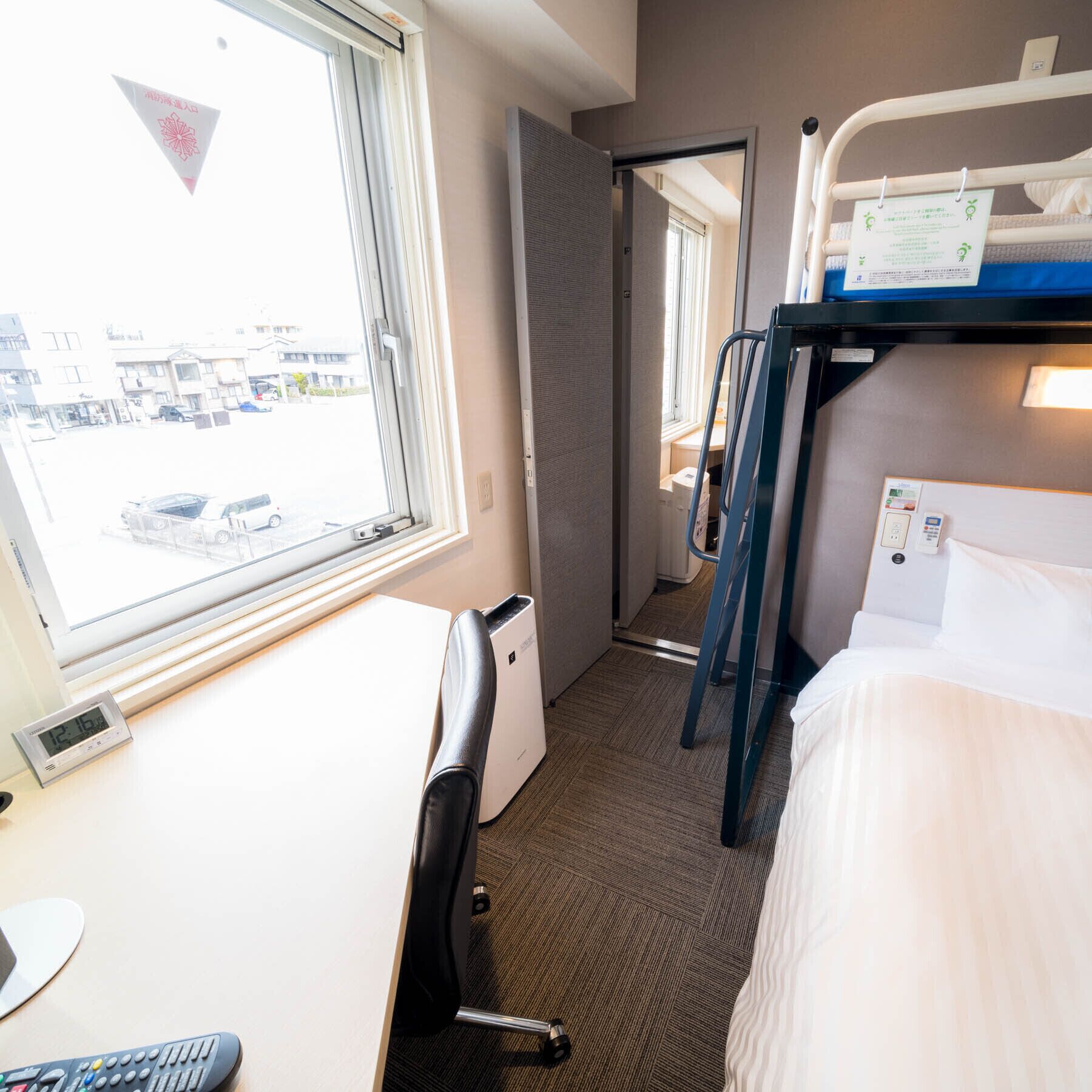 A hotel room with a bunk bed, a desk with a chair, a window, and a view of the outside.