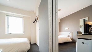 Ein Hotelzimmer mit zwei Betten, einem Schreibtisch mit Computer, einem Spiegel und einem Fenster.