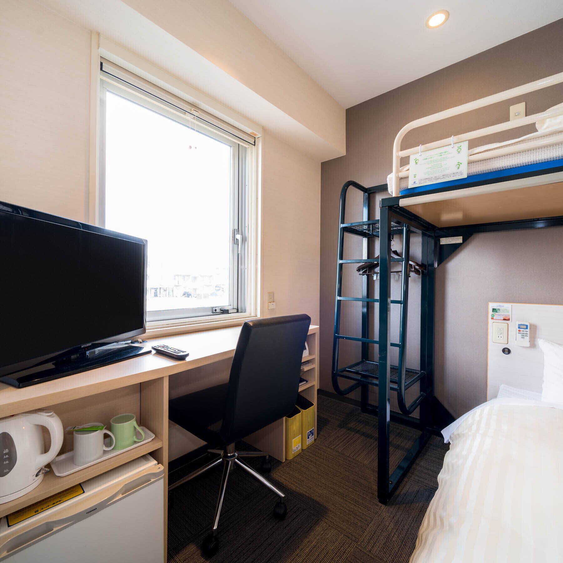 A hotel room with a desk, computer, chair, bunk beds, and a window.