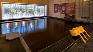 Ein traditionelles japanisches Onsen mit großem Fensterblick auf Bambus, geflieste Wände und einer hölzernen Sitzbank.