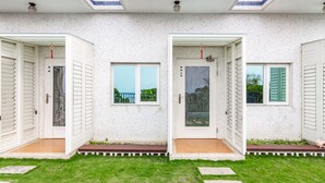 Une maison à deux étages avec des murs extérieurs blancs et un petit jardin à l’avant.