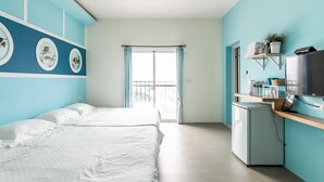 Une chambre avec un lit, une petite kitchenette, une télévision et une fenêtre avec des rideaux.
