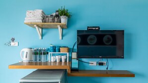 Une chambre d’hôtel moderne avec un mur bleu, un bureau en bois, une bouilloire, des tasses et un téléviseur.