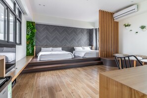 A modern hotel room with two beds, a wooden dining table, a built-in TV, and a green wall with plants.