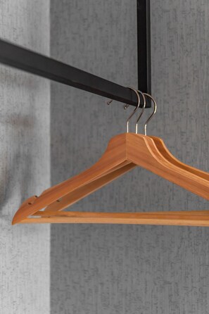 A wooden hanger suspended from a black metal rod against a textured wall.