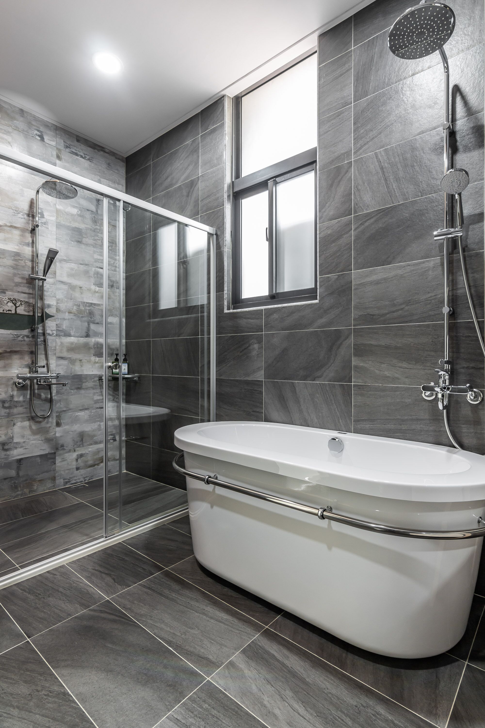 A modern bathroom with a freestanding bathtub, a glass-enclosed shower, and dark tiled walls.