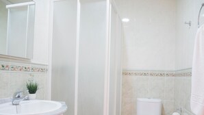 Une salle de bain avec un lavabo, des toilettes, une douche et une petite plante en pot.
