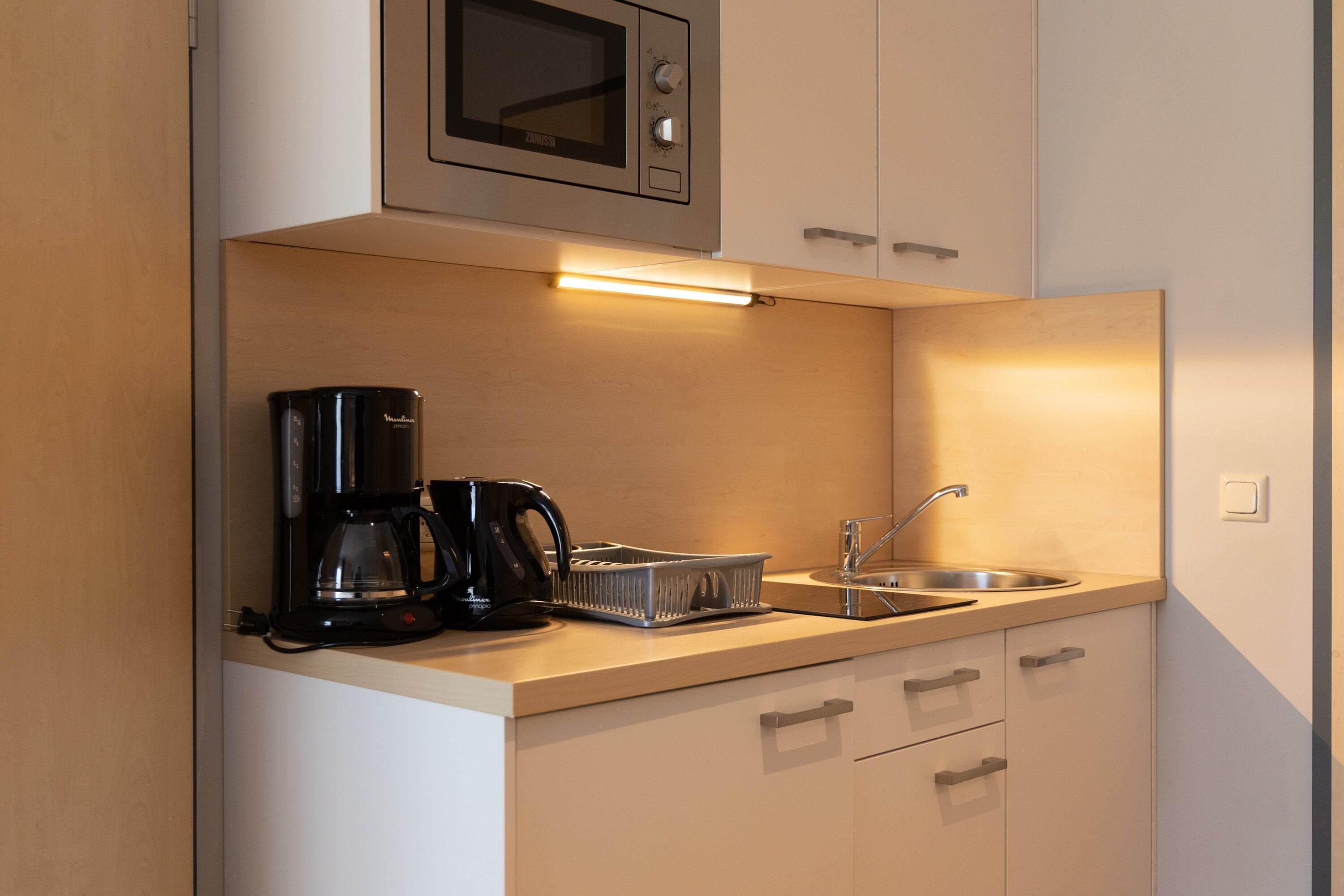 Een kleine keuken met een magnetron, koffiezetapparaat en een spoelbak.