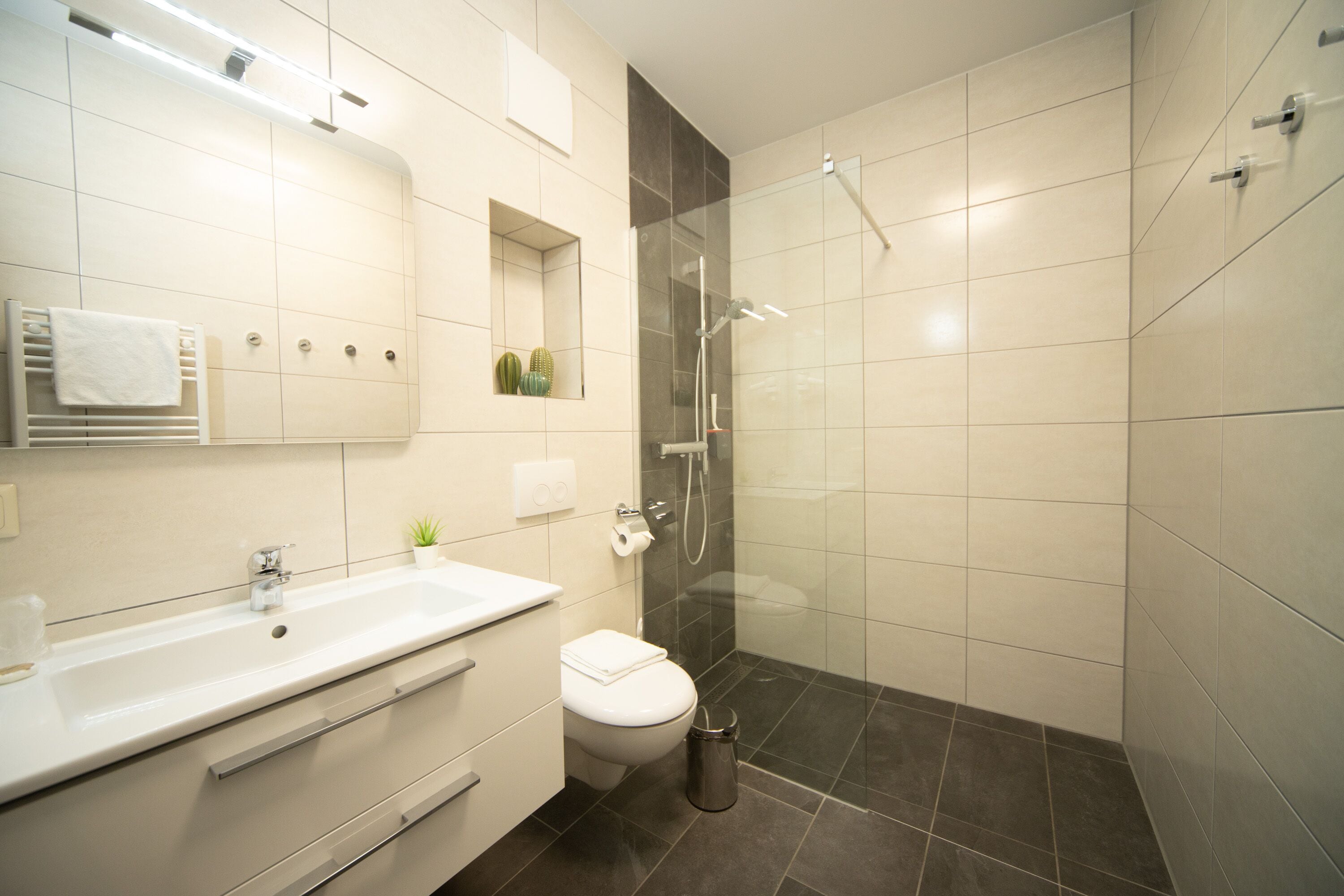Ein modernes Badezimmer mit Waschbecken, Toilette und Dusche, alles in Weiß.